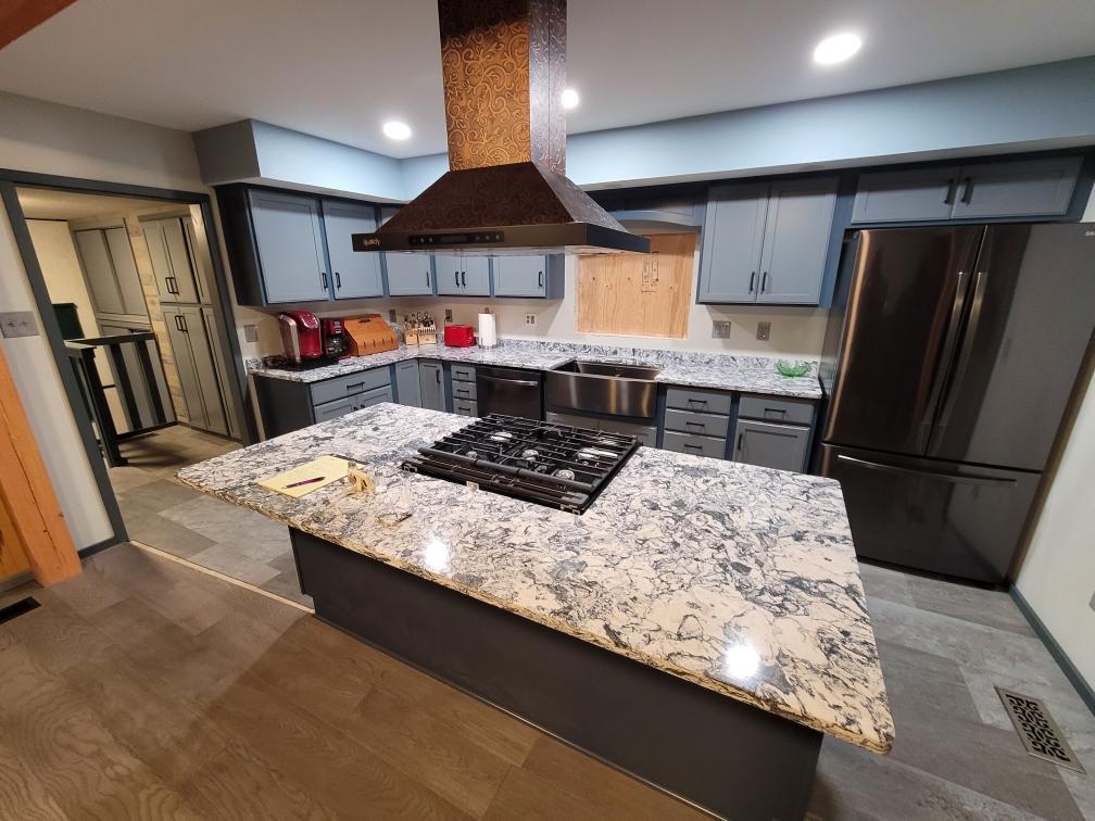 Kitchen with grey cabinet doors and a dark blue base cabinet color. A large center island with a marbled countertop.
